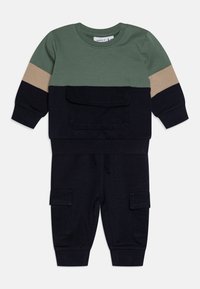 To-delt barneoutfit med en grønn og beige fargedelt overdel med lomme, og marineblå bukser med cargo-lommer og elastiske mansjetter.