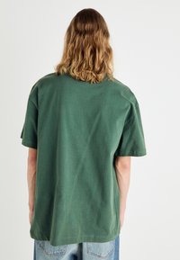 Camiseta verde de manga corta hecha de algodón. Corte holgado con cuello redondo, textura suave y diseño liso, mostrada desde la parte de atrás.