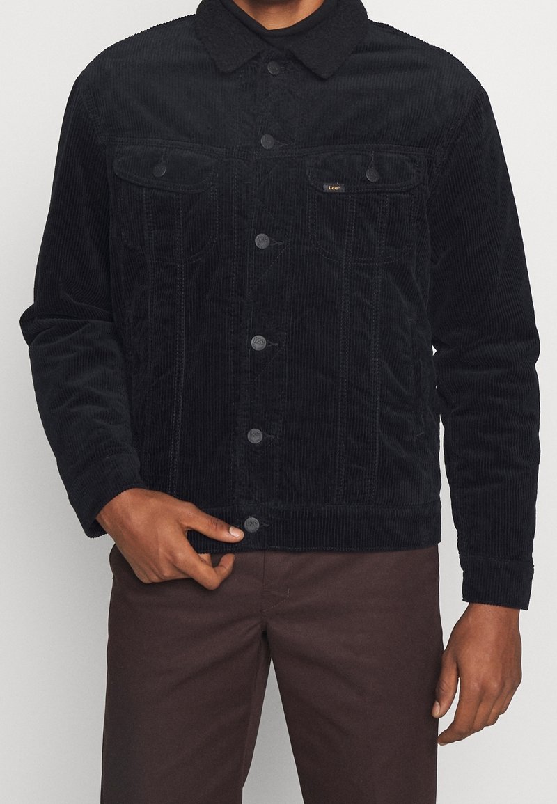 Veste en velours côtelé noire avec fermeture à boutons, col pointu et deux poches poitrine. Présente une texture côtelée et une coupe décontractée.