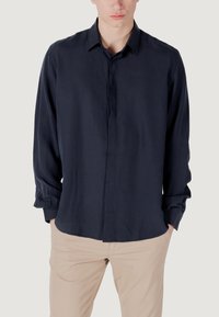 Navyblauwe knoopshirt van lichte, soepele stof. Voorzien van een klassieke kraag en lange mouwen met geknoopte manchetten.