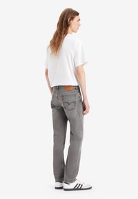 Grå jeans med en avsmalnande passform, med en läderpatch på baksidan, sydda detaljer och en sliten textur, tillsammans med en enkel vit t-shirt.