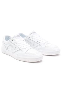 Une paire de baskets Vans blanches à tige basse avec des détails perforés, des lacets, et une languette et des panneaux latéraux de marque sur un fond blanc.