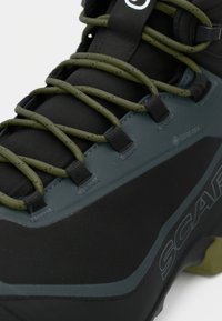 Crne planinarske čizme s teksturiranim površinom, sadrže zelene naglaske i Gore-Tex brendiranje. Uključuju izdržljive vezice i ojačane rupice za vezice.
