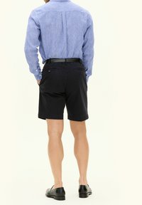 Niebiesko-biała w paski koszula na guziki, czarne szorty, slim fit, z tylnymi kieszeniami, noszona z czarnymi butami. Nogi widoczne z tyłu.