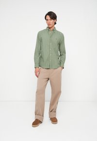 Groen-wit gestreepte overhemd met kraag, gecombineerd met beige broek en bruine schoenen. Eenvoudige, getailleerde pasvorm. Glad textuur.