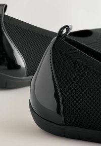 Schwarze Slipper mit strukturiertem, gestricktem Obermaterial und glänzenden Lacklederakzenten an der Ferse, ausgestattet mit einer flexiblen Gummisohle.