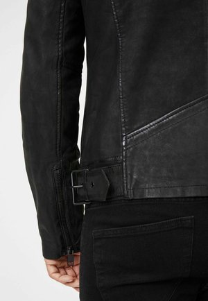 Schwarze Lederjacke mit einem Reißverschlussärmel, diagonalen Nahtdetails und einem taillierten Schnitt mit einer rechteckigen Schnalle. Glatte Textur.