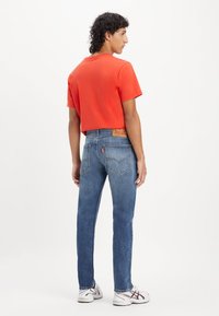 Kratka rdeča majica, modri naravni jeans z usnjenim blagom na pasu in bele superge z rdečimi in mornarsko modrimi detajli.
