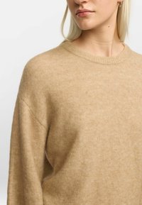 Beige Strickpullover aus weichem Material, mit Rundhalsausschnitt, gerippten Kanten und einer lockeren Passform mit dezenter Textur.