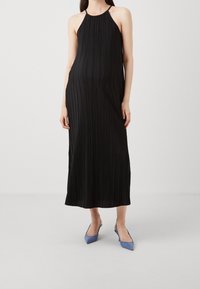 Czarna, sięgająca do kolan sukienka na ramiączkach z pionowymi fałdami; lekki materiał; modelka nosząca jasnoniebieskie, spiczaste szpilki.