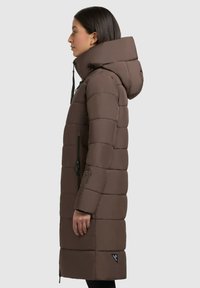 Braune Pufferjacke mit hohem Kragen, Kapuze und vertikalem Steppmuster. Verfügt über Reißverschlüsse an den Taschen und ein Logodetail am Saum.