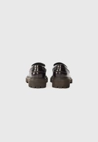 Sorte lærstøvler med en blank finish, med en tykk brun gummisåle og rund tå. Bakfra vises sømdetaljer og slip-on design.