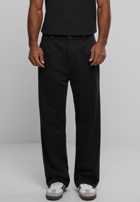Pantalones negros plisados con un corte ajustado, hechos de una tela suave, con bolsillos laterales y presillas para cinturón. Combinados con zapatillas blancas.