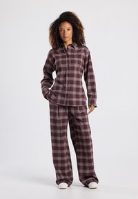 Karierte Pyjama-Set in Burgunderrot und Weiß, bestehend aus einer knöpfbaren Bluse und lockeren Hosen, hergestellt aus einem weichen Stoff mit glatter Textur.