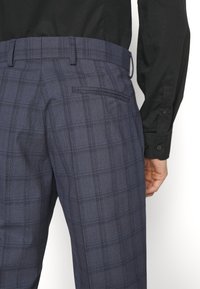 Navy checkered trousers with a textured fabric, featuring a single back pocket and a flat waistband. The pattern includes fine blue lines.