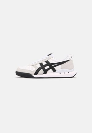 Athletic shoes with a white leather and gray suede upper, featuring black stripes, a thick rubber sole, and lace-up design.