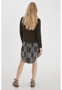 Olivegrüner Strickpullover, schwarz-weißer gestreifter Faltenrock und hellgraue Knöchelstiefel mit grünen Schnürsenkeln. Rückansicht angezeigt.