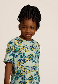 T-shirt à manches courtes de couleur vert clair avec un motif floral en jaune, bleu et vert. Il possède un col rond et une coupe décontractée.