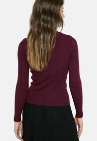 Burgundijas krāsas ribota džemperis ar garām piedurknēm, pieguļošs dizains, teksturēta auduma, valkāts ar melnu mežģīņu svārku, redzams aizmugurējais skats.