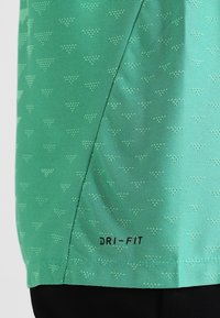 Camiseta deportiva DRI-FIT verde con un patrón texturizado de pequeños triángulos, fabricada en un tejido suave que absorbe la humedad y con letras en negro.