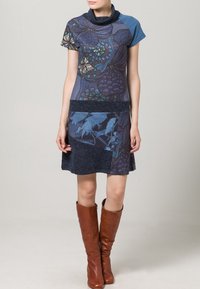 Robe bleue à manches courtes avec motifs floraux, col bénitier, corsage texturé, partie inférieure bleu foncé, assortie à des bottes marron montantes jusqu'aux genoux.