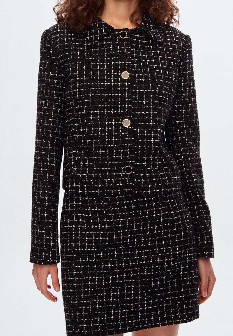 Zwart-wit geruit blazer met kraag, knopen aan de voorkant en een getailleerd silhouet, gecombineerd met een bijpassende rok. Gestructureerde stof.