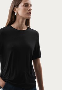 Zwarte T-shirt met korte mouwen van gladde stof en een ronde halslijn, gecombineerd met donkere spijkerbroeken. Eenvoudig ontwerp met een ontspannen pasvorm.