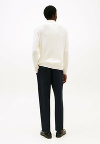 Biała teksturowana sweter z pulowerem z ribbowanymi mankietami, w połączeniu z granatowymi spodniami. Prosty design, luźny krój i minimalne akcenty hardware.