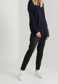 Top de manga larga azul marino con cuello a rayas, combinado con pantalones ajustados gris oscuro y zapatillas blancas. La parte superior tiene aberturas laterales para una mayor movilidad.
