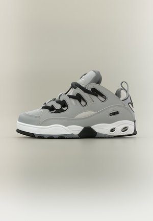 Baskets basses gris et blanc avec lacets noirs, semelle épaisse et logo de la marque sur le côté, montrées sur un fond neutre.