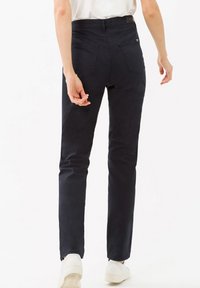 Pantaloni aderenti blu scuro realizzati in tessuto misto cotone, con tasche posteriori e una texture liscia. Indossati con scarpe bianche.