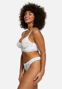 Conjunto de lencería blanca de encaje que incluye un sujetador tipo bralette con patrones florales y bordes festoneados, complementado con un hilo dental a juego con detalles similares.