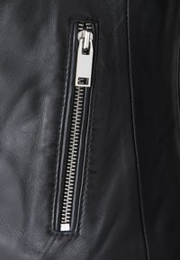 Tessuto in pelle nera con una vista ravvicinata di una cerniera argentata, caratterizzata da accessori metallici e una texture liscia, cucita ordinatamente lungo il bordo.