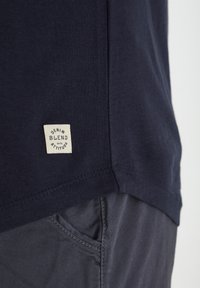 Mornarsko plava majica od mekane pamučne mješavine, s kvadratnom etiketom ušivenom na rubu koja glasi "DENIM MJEŠAVINA S STAVOM."