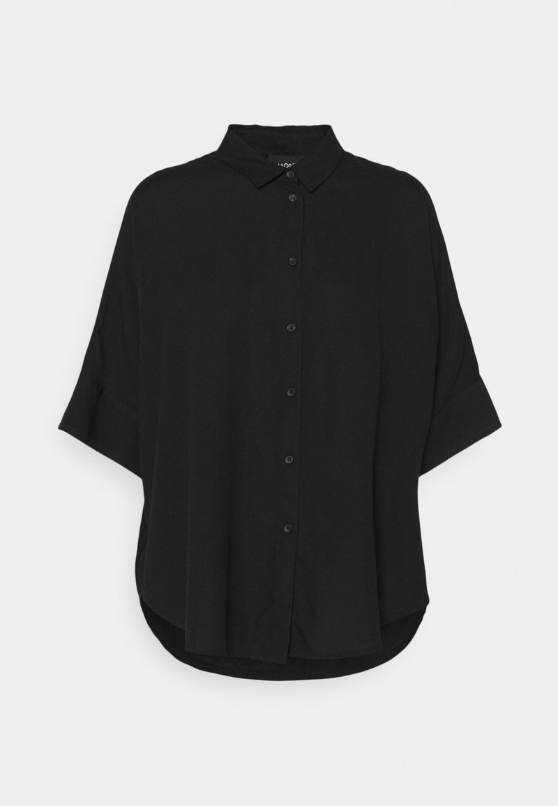Chemise noire oversize à boutons, en tissu doux, avec col, manches courtes et ourlet incurvé. Aucune imprimé ni accessoire visible.
