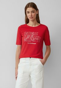 Rode katoenen T-shirt met korte mouwen en een ronde halslijn. Bevat witte grafische tekst: "SHINE BRIGHT CHASE DREAMS" met accentueringen. Witte broek.