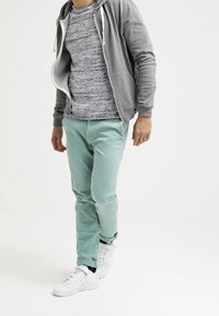 Šedá mikina na zip přes skvrnitý šedý tričko, v kombinaci s mátově zelenými kalhotami a bílými teniskami. Jednoduchý, ležérní design.