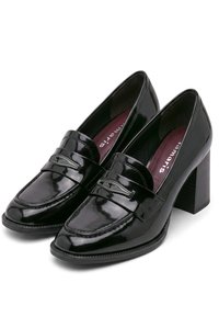Λουστραρισμένα μαύρα δερμάτινα loafers με ψηλό τακούνι και διακοσμητικό ραφτό, εμφανιζόμενα από κεκλιμένη κορυφαία όψη.