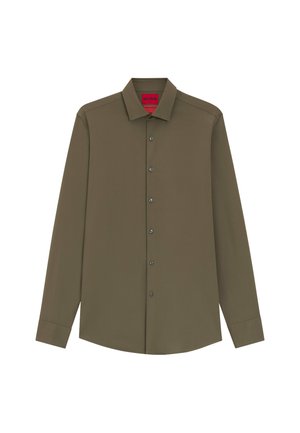 Camisa de manga larga color verde oliva con cuello abotonado, con botones negros y una etiqueta roja en el interior del cuello. Textura suave.