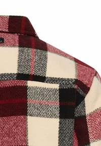 Flannel skjorte med et mønster i røde, sorte og creme farver. Fremstillet af blødt stof med spids krave og lomme detalje.