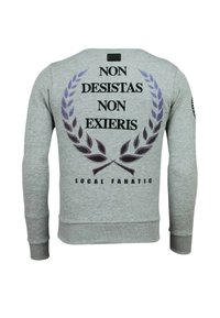 Grijze sweatshirt met lange mouwen met zwarte tekst "NON DESISTAS NON EXIERIS," paars lauwerkransgrafiek en "LOCAL FANATIC" onderaan aan de achterkant.