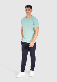 Camiseta de manga corta verde menta combinada con joggers azul marino. Los joggers presentan un logo sutil y están hechos de un tejido suave. Zapatillas deportivas blancas.