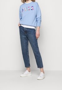 Ljusblå kort sweatshirt med flerfärgad "POLO" broderad text, i kombination med medelhöga mörkblå avslappnade jeans och vita sneakers.