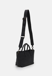 Svart handväska med strukturerat material, dubbla handtag och en avtagbar axelrem med präglad märkning längs hela remmen.