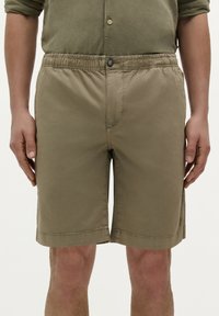 Pantaloni scurți bej, până la genunchi, dintr-un material ușor, cu un tiv elastic și un singur nasture de închidere în față.