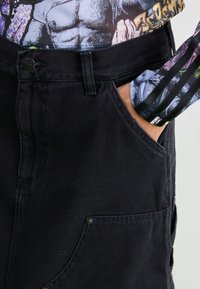 Høytlivte sorte denimbukser med sidelommer, kontraststing og en jevn tekstur. Har knappelukking og solid stoff.