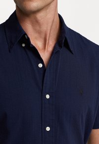Camicia a maniche corte slim fit di colore blu navy, realizzata in tessuto testurizzato, con colletto a punta e bottoni bianchi, decorata da un discreto logo sul lato sinistro del petto.
