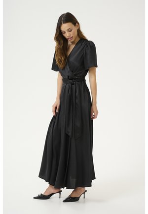 Black wrap dress with a cinched waist, short puff sleeves, and a flowing skirt. Worn with black high-heeled mules featuring decorative hardware.