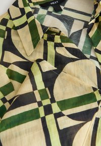 Chemise boutonnée en tissu léger et texturé présentant un motif géométrique en vert, noir et crème avec un col classique.
