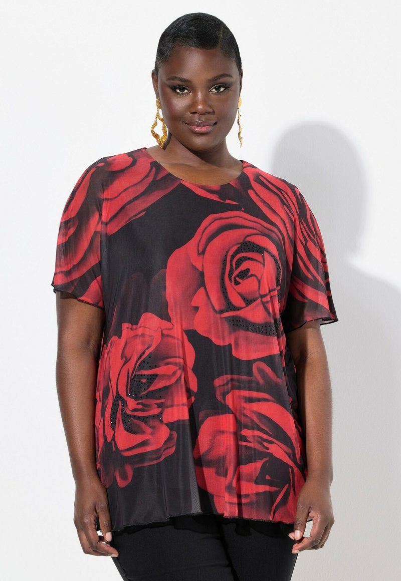 Top nero con grande stampa di rose rosse, maniche corte, scollo rotondo, tessuto trasparente e orlo ondulato. Abbinato a pantaloni neri.